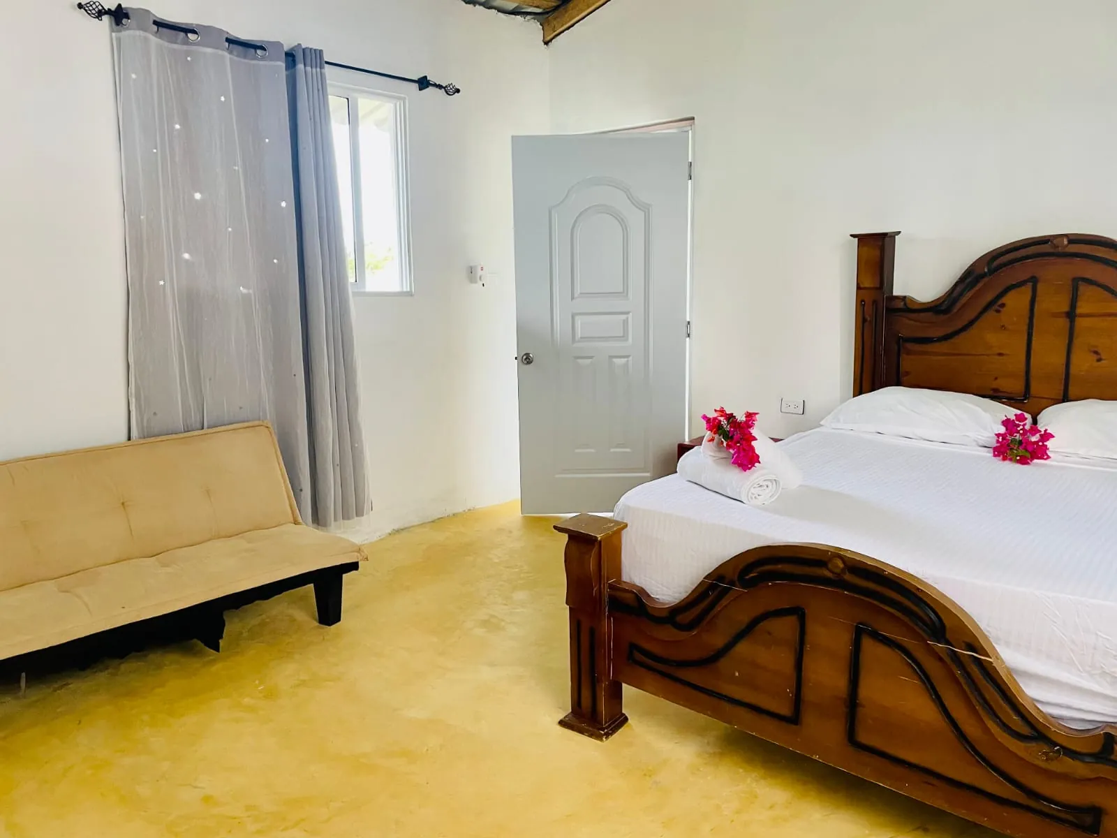 Bedroom with a large wooden bed, white sheets and a sofa