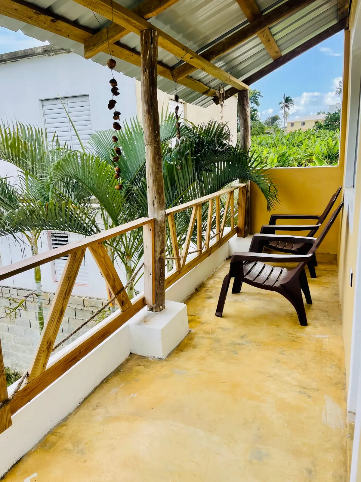 Covered balcony with wooden railing, chairs and palms