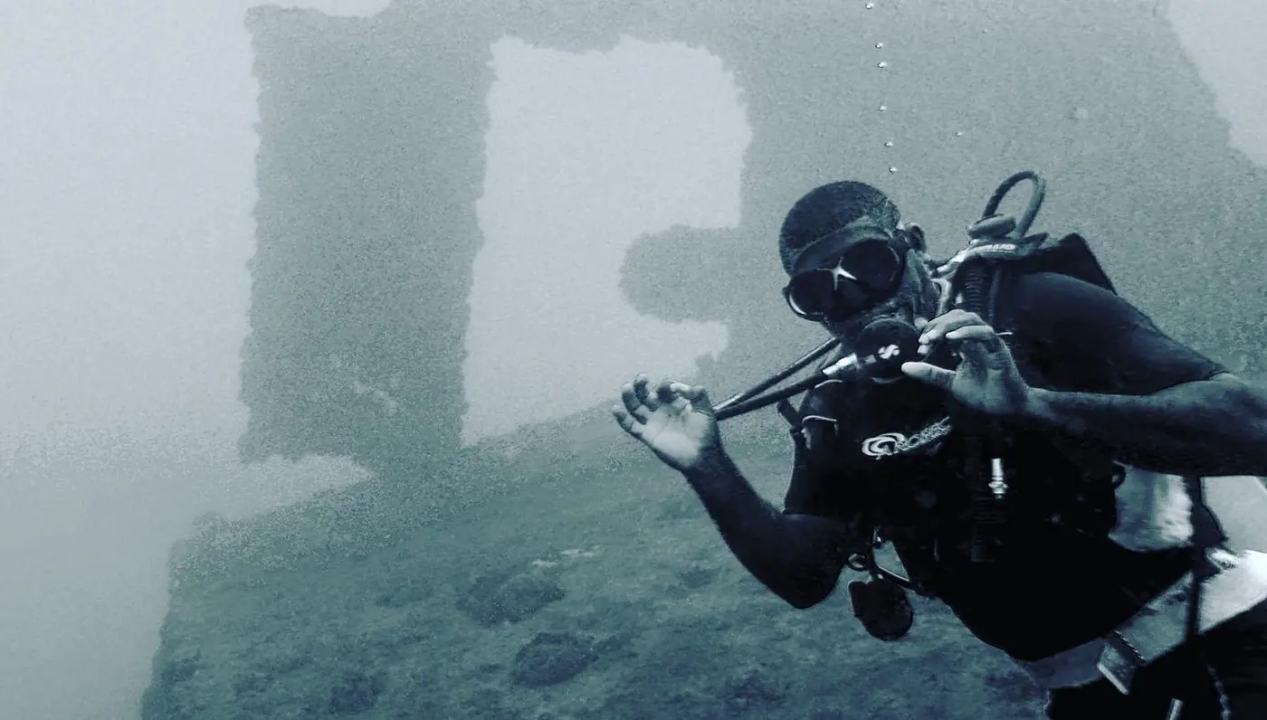 Diver giving the OK sign in front of a wreck